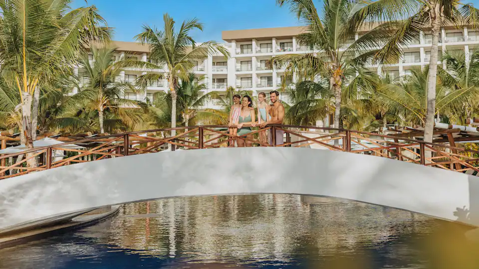 Family standing on a bridge overlooking the resort pools and tropical grounds at Hyatt Ziva Cap Cana in Punta Cana.