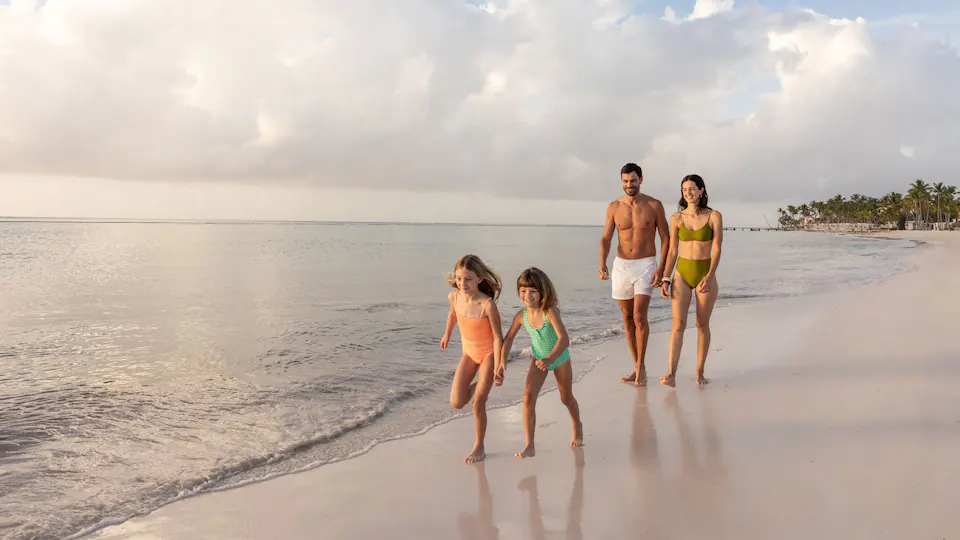 Family walking along the white-sand beach at Hyatt Ziva Cap Cana with calm Caribbean waters and tropical scenery.
